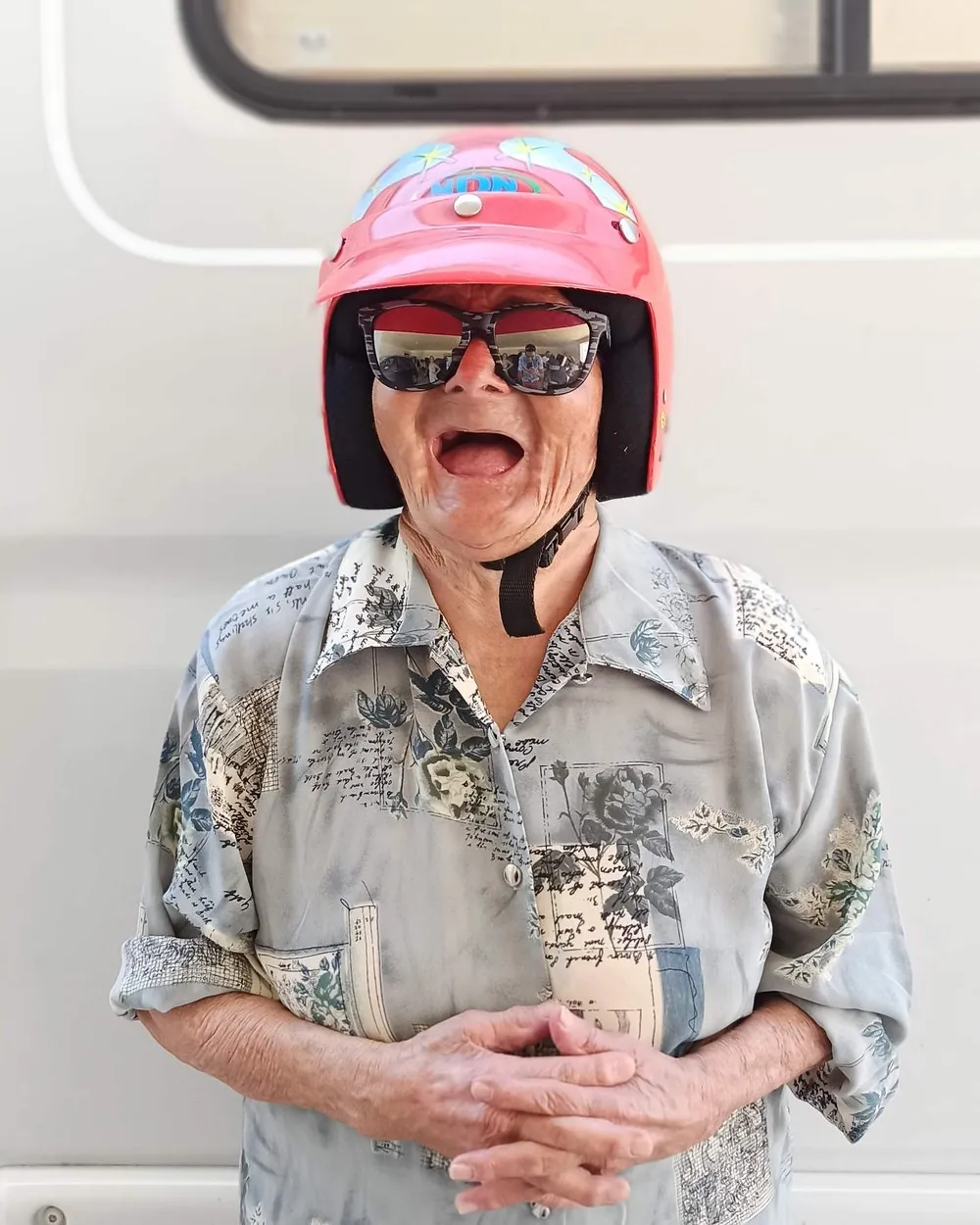 A Maria a rir às gargalhadas, com um capacete de mota cor-de-rosa e óculos escuros.